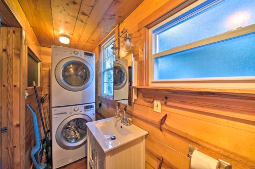 A cozy laundry room featuring stacked washer and dryer, a sink, and wooden walls with a window for natural light.