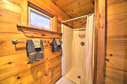 A rustic bathroom with wooden walls, a shower stall, and two gray towels hanging on a rack.