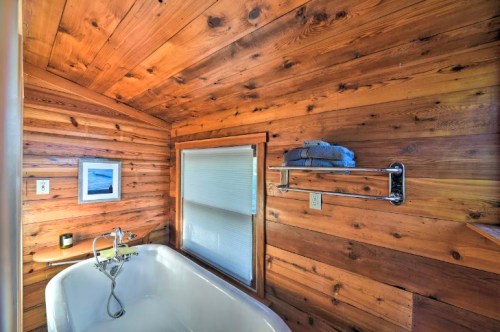 Cozy bathroom with wooden walls, a vintage bathtub, and a towel rack with neatly folded towels. Natural light from a window.