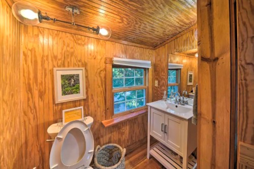 A cozy bathroom with wooden walls, a white vanity, a mirror, and a window letting in natural light.