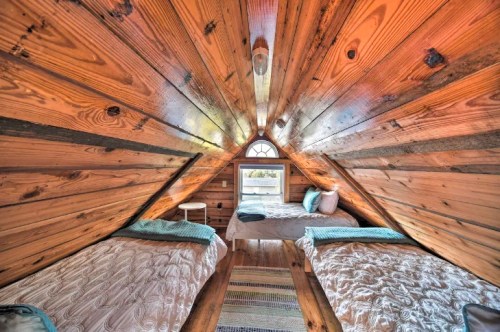 Cozy attic bedroom with wooden walls, two beds, and a window, creating a warm, inviting atmosphere.