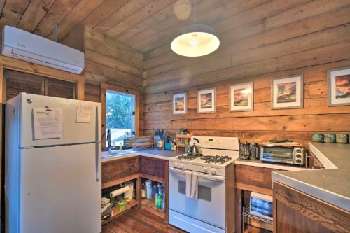 Cozy wooden kitchen with a fridge, stove, and framed pictures on the wall, featuring warm lighting and rustic decor.