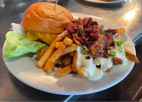 A plate featuring a burger with lettuce and a side of loaded fries topped with bacon and green onions.