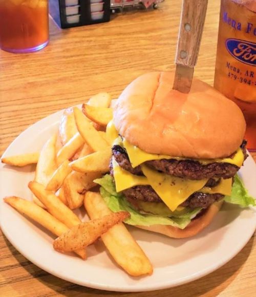 A large cheeseburger with three patties, lettuce, and cheese, served with a side of golden fries on a white plate.