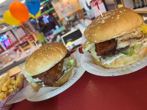 Two burgers on a tray, one with fried chicken and the other with a fried egg, alongside a serving of fries.
