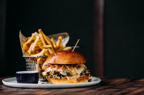 A gourmet burger with melted cheese and toppings, served with a side of crispy fries in a small basket.