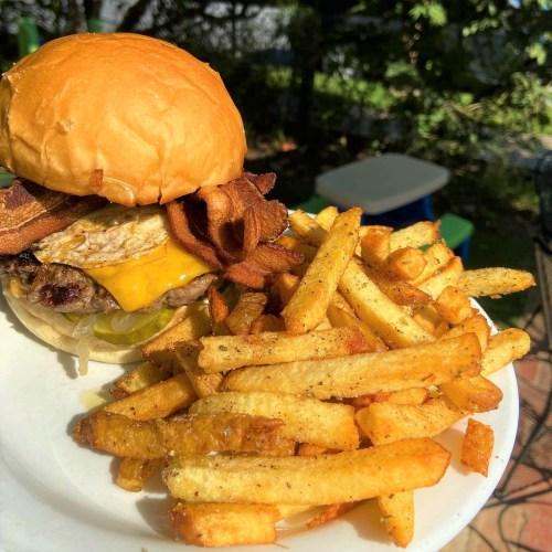 A juicy burger with cheese, bacon, and a fried egg, served with a side of crispy golden fries on a plate.