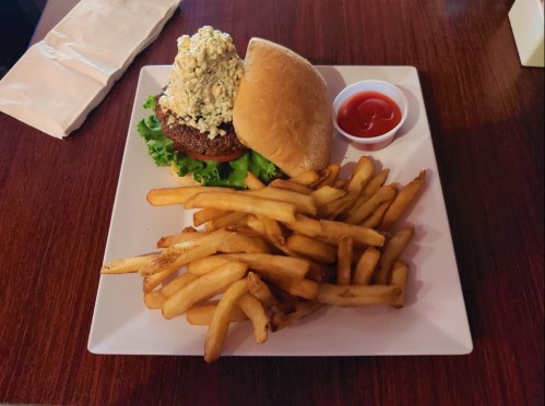 A plate with a burger topped with a creamy mixture, lettuce, and a side of golden fries and ketchup.