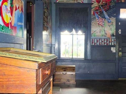 Interior of a room with dark blue walls, a window, and a wooden table, featuring colorful murals and American flags.