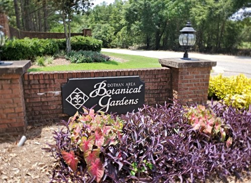 Sign for Dothan Area Botanical Gardens, surrounded by colorful plants and greenery.