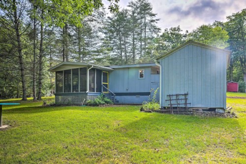 A blue house with a screened porch and a small shed, surrounded by green grass and trees under a cloudy sky.