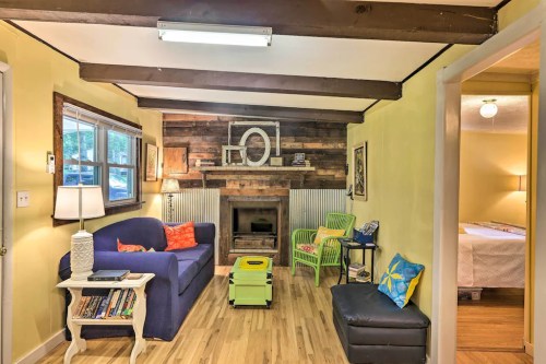 Cozy living room with a blue sofa, wooden beams, a fireplace, and colorful decor, leading to a bedroom.