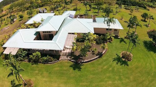 Aerial view of a spacious, modern house surrounded by lush green lawns and tropical trees.