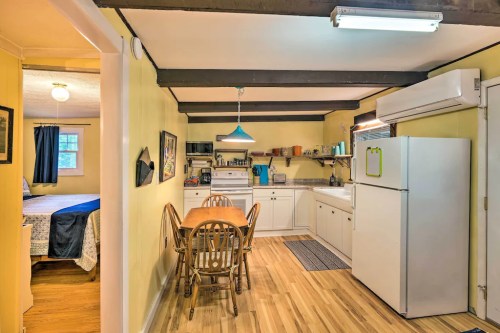 Cozy kitchen with wooden beams, dining table, white appliances, and a view into a nearby bedroom.