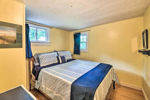 Cozy bedroom with a large bed, yellow walls, and two windows, featuring blue curtains and wooden flooring.