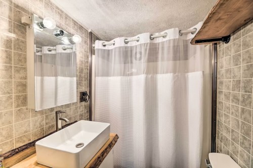A modern bathroom featuring a shower with a curtain, a sink on a wooden countertop, and tiled walls.