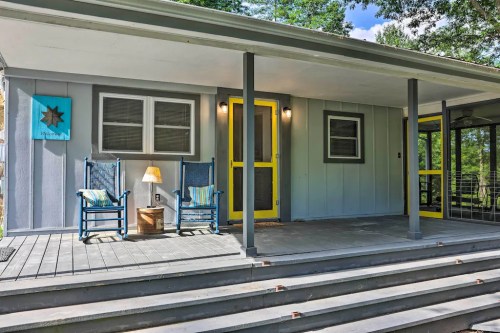 A cozy porch with two rocking chairs, a lamp, and a bright yellow door, surrounded by greenery.