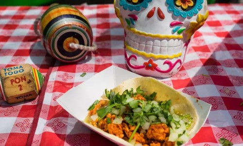 A colorful sugar skull beside a taco topped with cilantro and onions on a red checkered tablecloth.