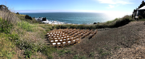 A scenic outdoor wedding setup with rows of chairs overlooking the ocean and a clear blue sky.