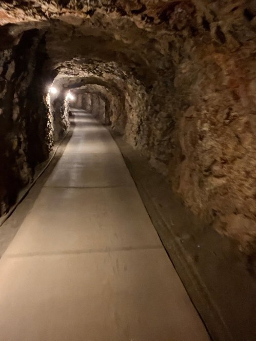 A dimly lit underground tunnel with rocky walls and a smooth concrete path.