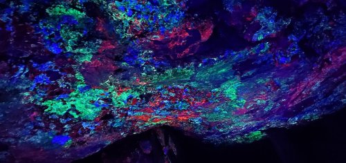 Vibrant, multicolored patterns on a cave ceiling, illuminated in shades of blue, green, and red.