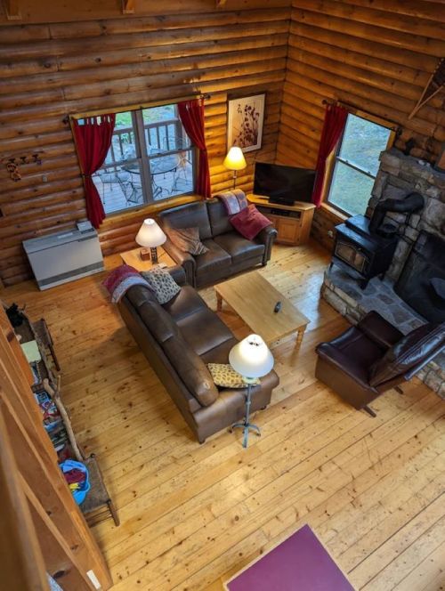 Cozy log cabin living room with wooden floors, two sofas, a coffee table, and a stone fireplace. Warm lighting and decor.