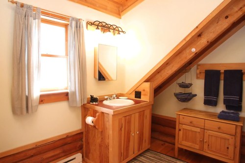 Cozy bathroom with wooden accents, a sink, mirror, and towels, featuring a sloped ceiling and natural light.