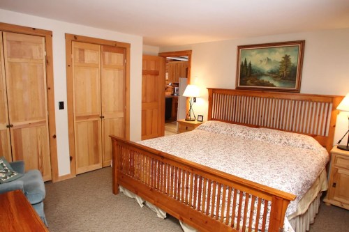 Cozy bedroom with a wooden bed, floral bedding, lamps, and closet doors, featuring warm lighting and a mountain painting.