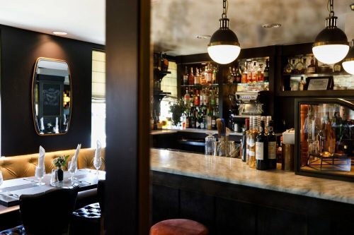 A stylish bar area with a marble countertop, shelves of liquor, and elegant lighting in a cozy restaurant setting.
