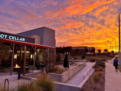 A vibrant sunset casts orange and pink hues over a building with outdoor seating and a pathway.