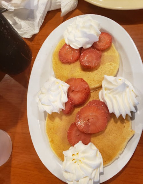 Two pancakes topped with strawberries and dollops of whipped cream, served on a white plate.
