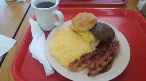 A plate with scrambled eggs, bacon, sausage, a biscuit, and a cup of coffee on a red tray.