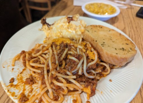 A plate of spaghetti with meat sauce, macaroni and cheese, and a slice of garlic bread.