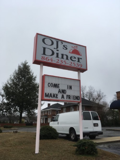 Sign for OJ's Diner inviting customers to "Come in and make a friend," with a white van parked nearby.