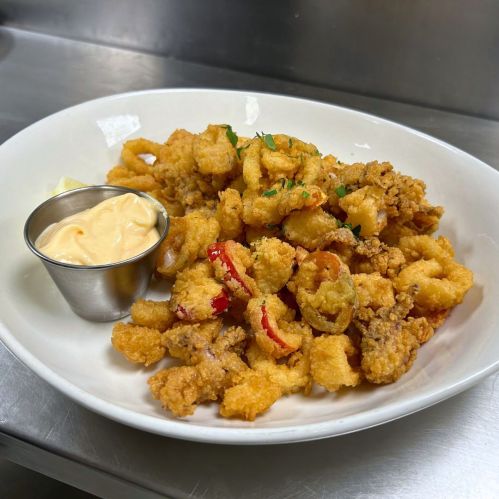 A plate of crispy fried calamari with sliced peppers, garnished with parsley, and a side of dipping sauce.