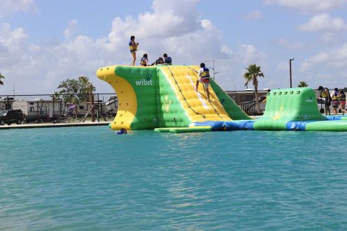 A colorful inflatable water slide with people climbing and playing in a pool under a blue sky with fluffy clouds.