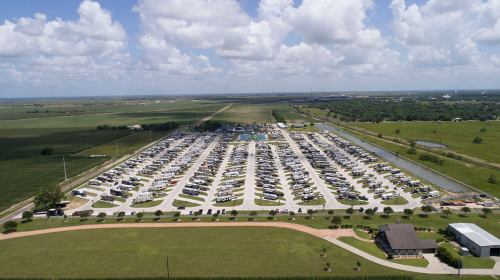 Aerial view of a large RV park with numerous parked vehicles, surrounded by green fields and a blue sky with clouds.