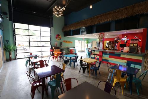 Colorful café interior with tables and chairs, a vibrant counter, and large garage door open to the outside.