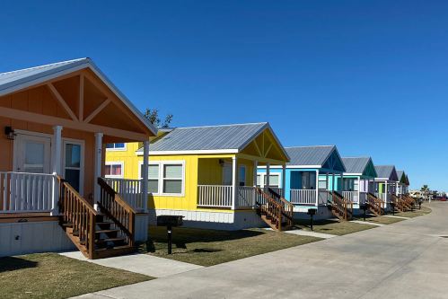 Colorful small houses with porches line a sunny street under a clear blue sky.