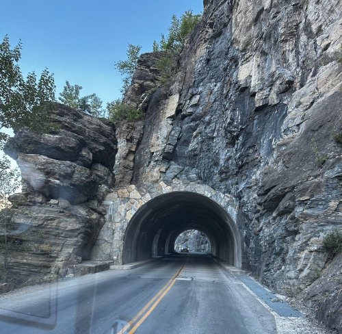 A scenic view of a tunnel carved through rocky cliffs, with a clear blue sky above and a road leading through it.