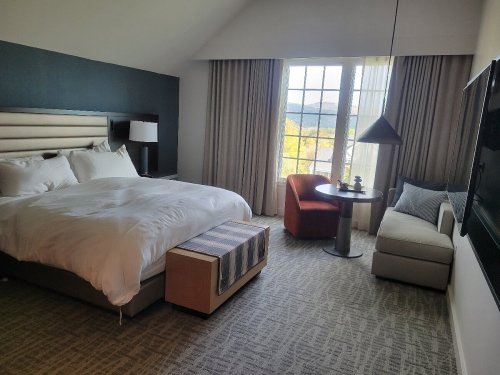 Modern hotel room featuring a large bed, seating area, and large windows with a view.