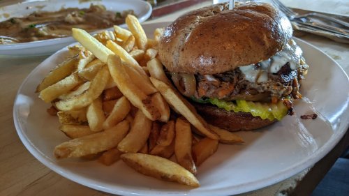 A hearty burger with lettuce, pickles, and sauce, served with a side of golden French fries on a white plate.