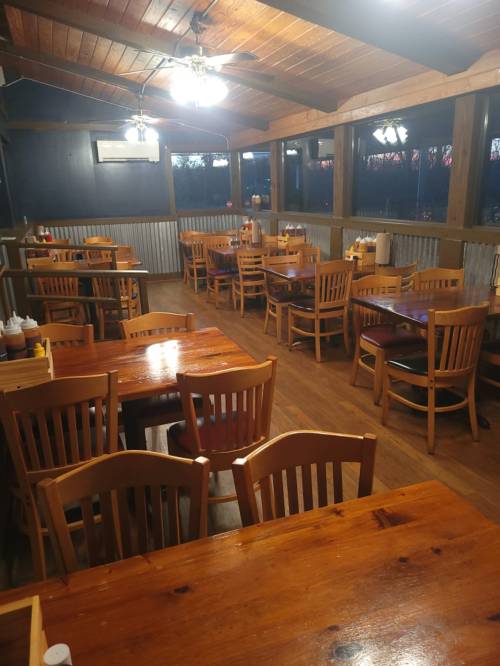 A cozy restaurant interior with wooden tables and chairs, featuring a rustic ceiling and large windows.