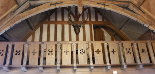 Wooden balcony with decorative carvings and a mounted deer head, set in a rustic, timber-framed interior.