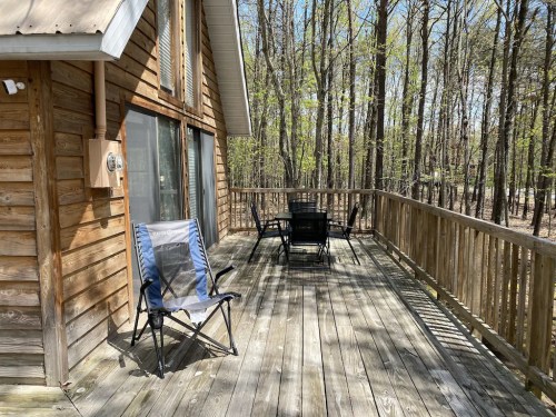 A wooden deck with two chairs and a table, surrounded by trees on a sunny day.