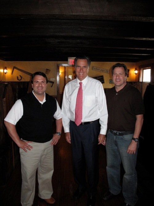 Three men pose together in a rustic restaurant setting, smiling for the camera.