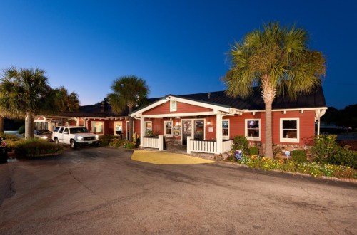 A red building with palm trees, parked cars, and a clear blue sky at dusk.