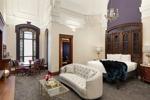 Elegant hotel room featuring a plush bed, vintage furniture, a cozy seating area, and a stained glass window.