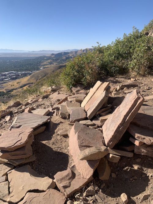 Rock formations on a hillside with a view of a valley and distant mountains under a clear blue sky.