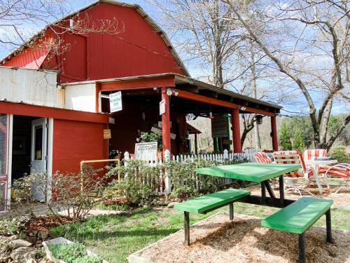 A red barn-style building with outdoor seating and picnic tables, surrounded by trees and greenery on a sunny day.